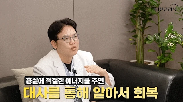 흰 의사 가운을 입은 남성 의사가 검은 소파에 앉아 손으로 제스처하며 설명하고 있다. 흉살 회복 원리를 다루는 비절개흉살치료레이저 관련 설명 화면.